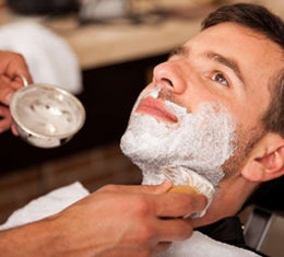 A barber applying warm shaving lather to a client